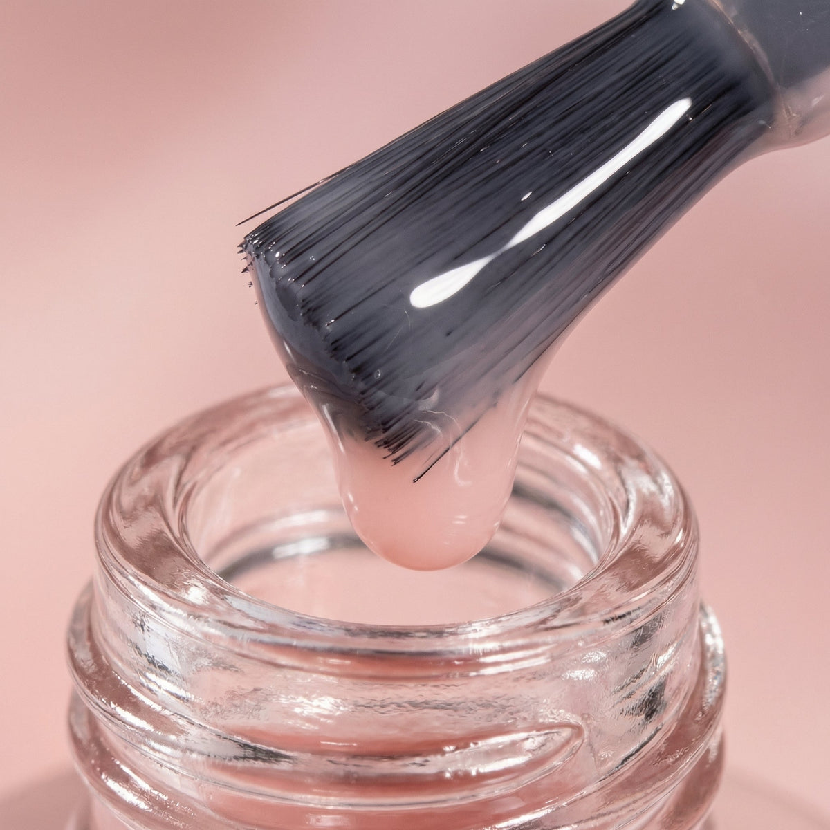 Pensula lată scoasă din sticluță, cu lac roz transparent care se scurge