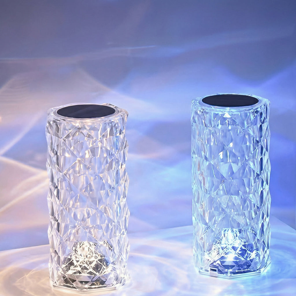 Două lămpi cu aspect de cristal aprinse, cu reflexii de lumină pe masă