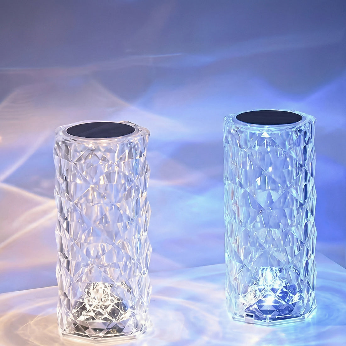Două lămpi cu aspect de cristal aprinse, cu reflexii de lumină pe masă