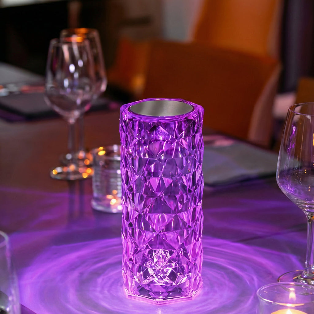 Lampă LED cu aspect de cristal în lumină mov, pe o masă cu pahare